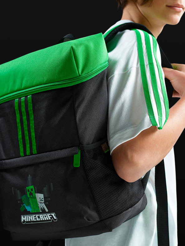A person wearing a black and white striped shirt is carrying a green and black backpack with the Minecraft logo on it.