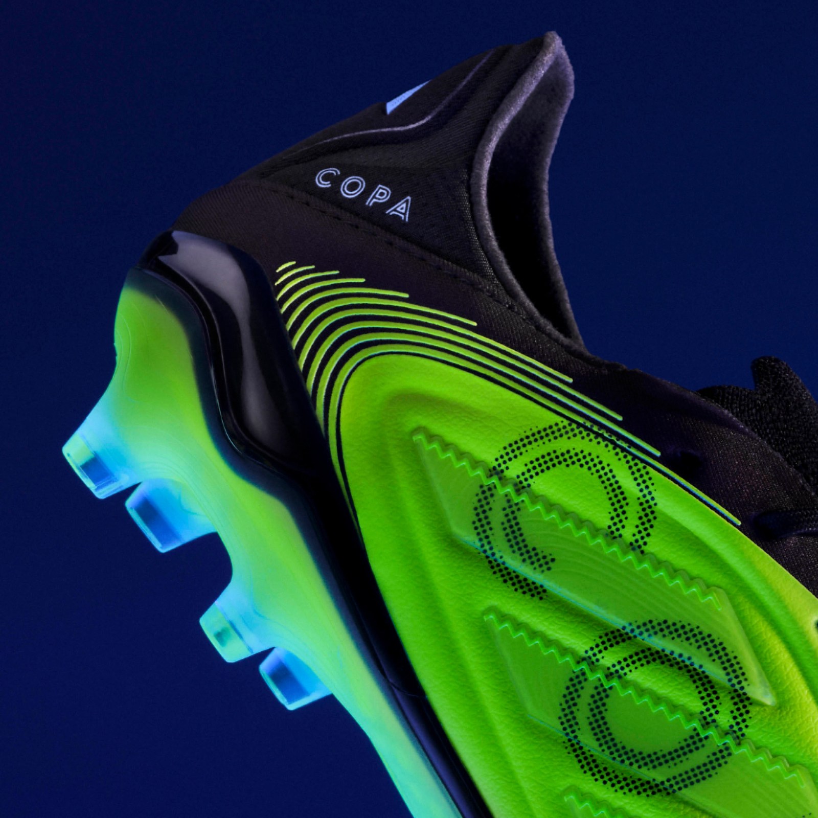 A black and green soccer cleat with the "Copa" logo stands out against a dark blue background.