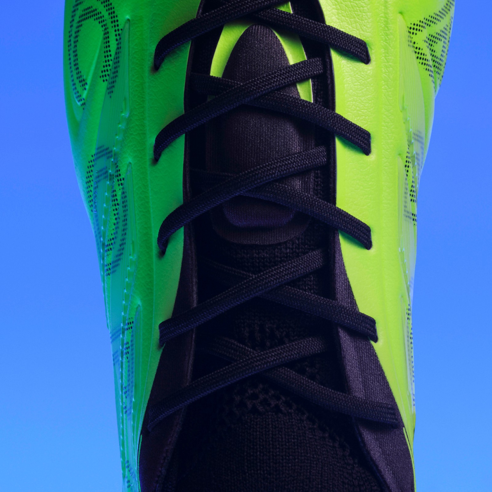 Vibrant green athletic shoe with black laces and trim against a bright blue background.