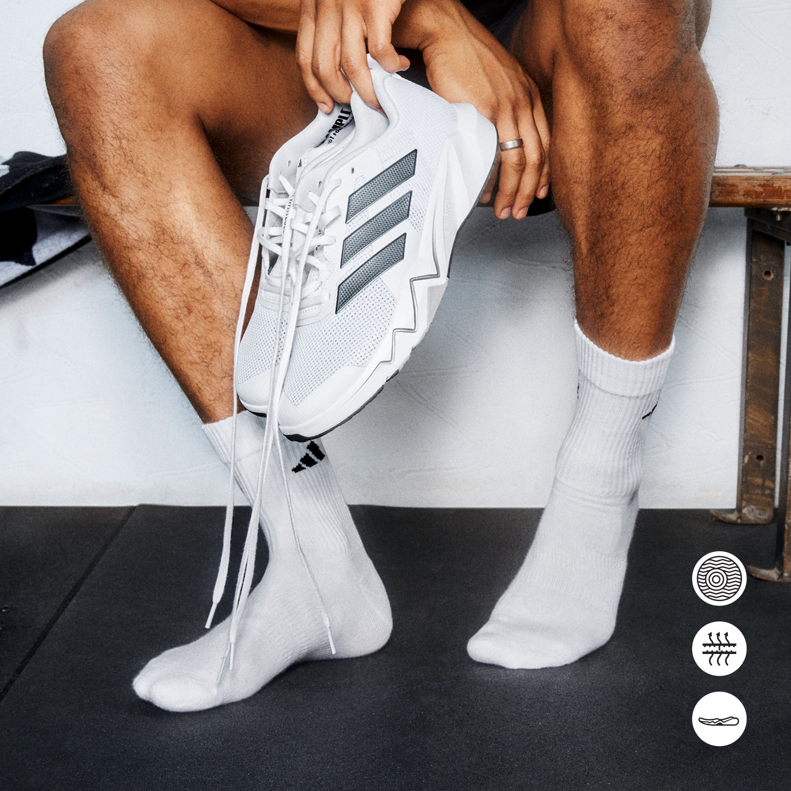 The image shows a person's lower body and feet, wearing white athletic shoes and socks, sitting on a surface against a plain background.