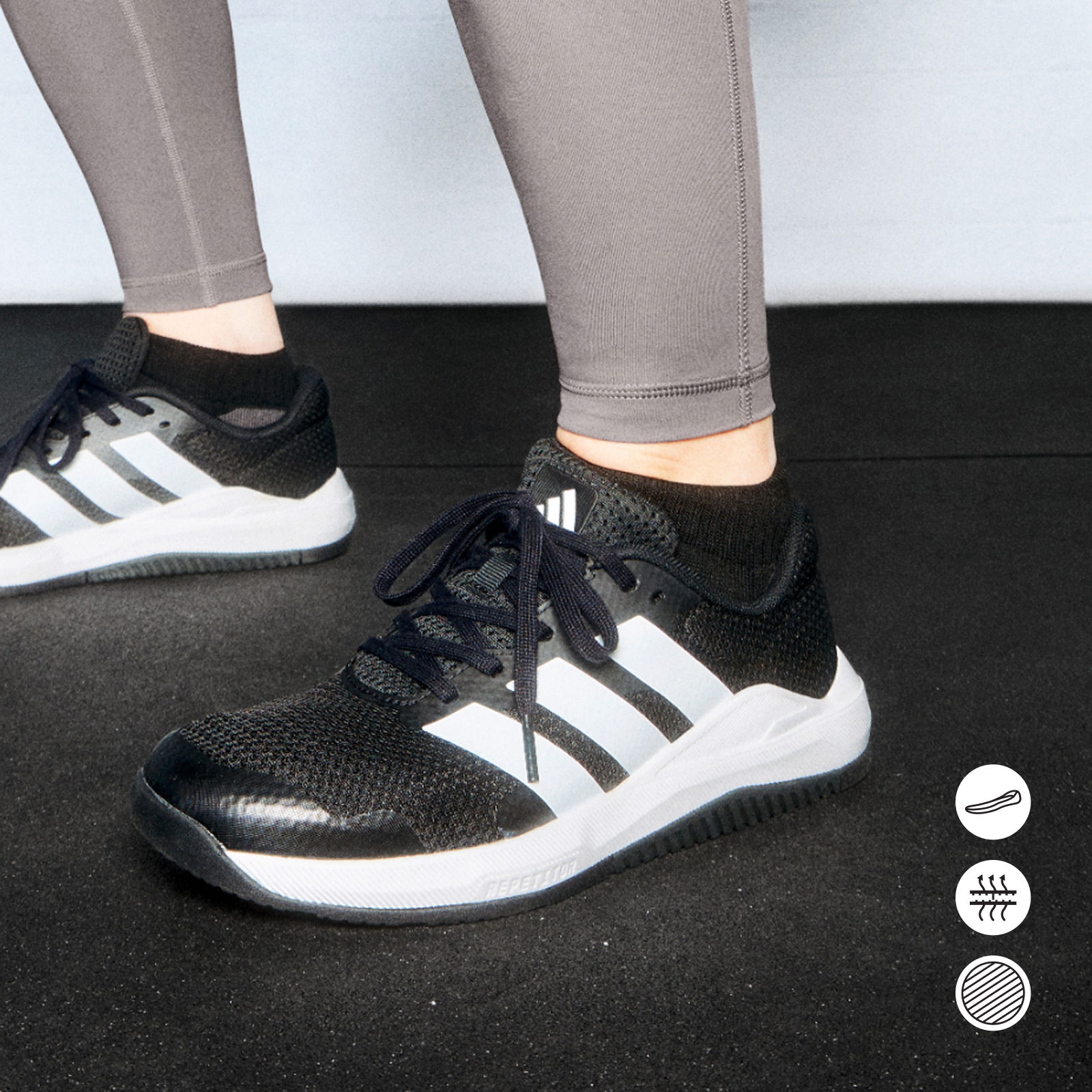 Na obrázku je pár černobílých sportovních bot na nohou člověka, přičemž nohy a kalhoty jsou viditelné v popředí na tmavém pozadí.