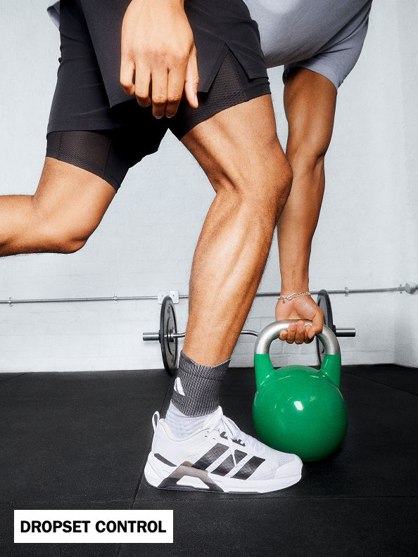 The image shows a person's lower body wearing athletic clothing and shoes, holding a green kettlebell in a gym or fitness setting.