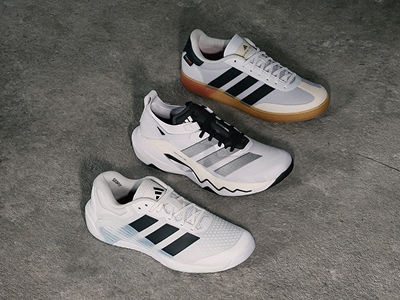 Three pairs of white and black athletic shoes with gum soles are displayed on a grey concrete surface.
