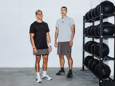 Dos hombres de pie en un gimnasio, con un equipo de ejercicios visible en el fondo.
