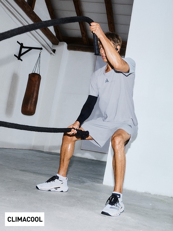 Una persona vestida con ropa deportiva está realizando una rutina de entrenamiento en el gimnasio con varios equipos de ejercicios visibles de fondo.