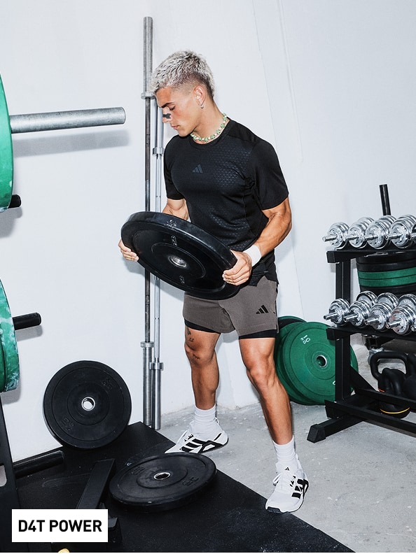 A person in a black shirt and shorts is lifting a heavy barbell in a gym setting, surrounded by various exercise equipment.