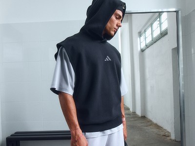 A person wearing a black hooded sweatshirt stands in a hallway with white walls and windows.