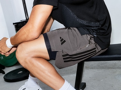 The image shows a person's lower body wearing black clothing and grey athletic shorts, sitting on a chair in what appears to be a studio or office setting.