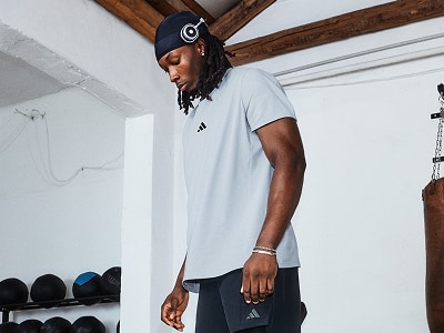 A young man wearing a white t-shirt and headphones stands in a room with wooden beams on the ceiling.