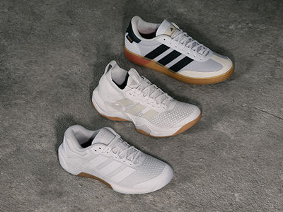 Three pairs of white and black trainers with gum soles are displayed on a grey concrete surface.