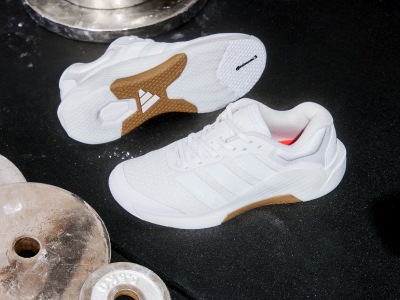 A pair of white trainers with a gum sole and a distinctive design on the side, set against a dark background with various other objects.