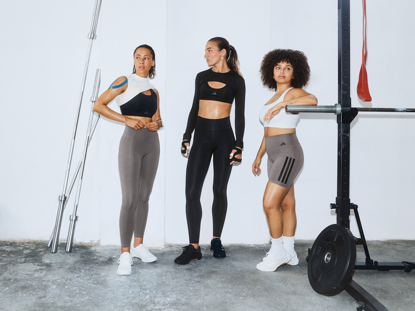 Tre donne in abbigliamento sportivo posano in un ambiente di fitness studio con attrezzatura per l'allenamento sullo sfondo.