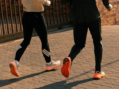 Due persone che indossano leggings sportivi neri e sneaker arancioni brillanti sono in piedi su una superficie lastricata di mattoni in un ambiente outdoor.