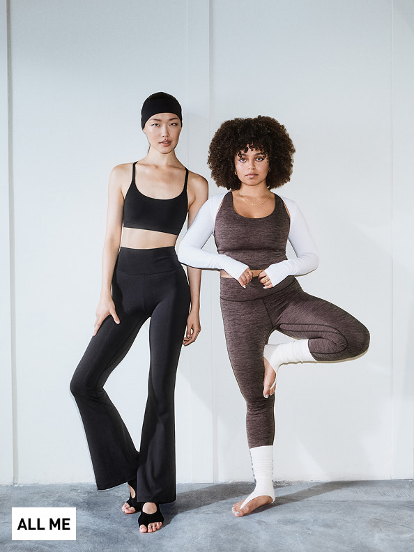 Dos mujeres con ropa deportiva posan en un estudio minimalista, una con pelo liso y la otra con pelo rizado, ambas posando con confianza.