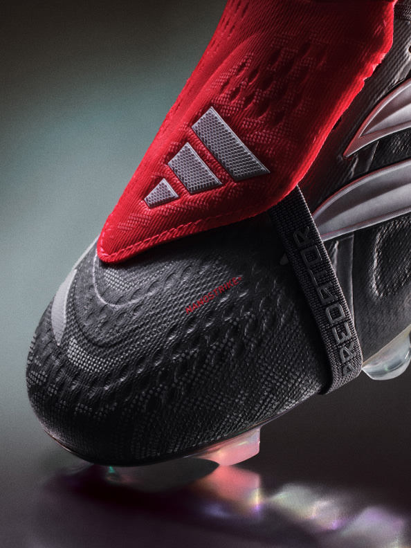 A close-up view of a red and black athletic shoe with a distinctive treaded sole, set against a dark background.