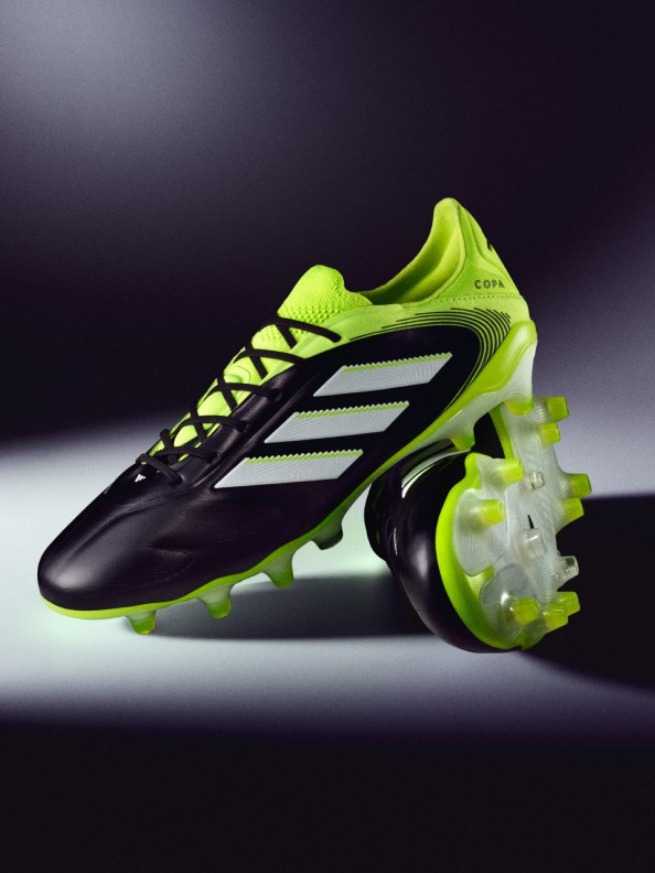 The image shows a pair of black and neon green soccer cleats on a dark background, with the cleats prominently displayed in the foreground.