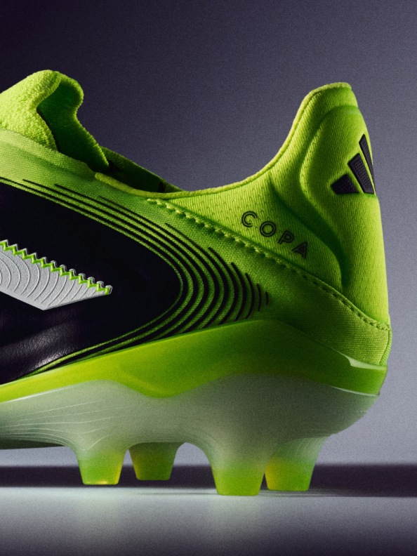 A vibrant green soccer cleat with a sleek, aerodynamic design stands out against a dark background, showcasing its striking visual appeal.