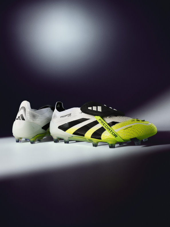 A pair of white and yellow soccer cleats rests on a reflective surface against a dark background.