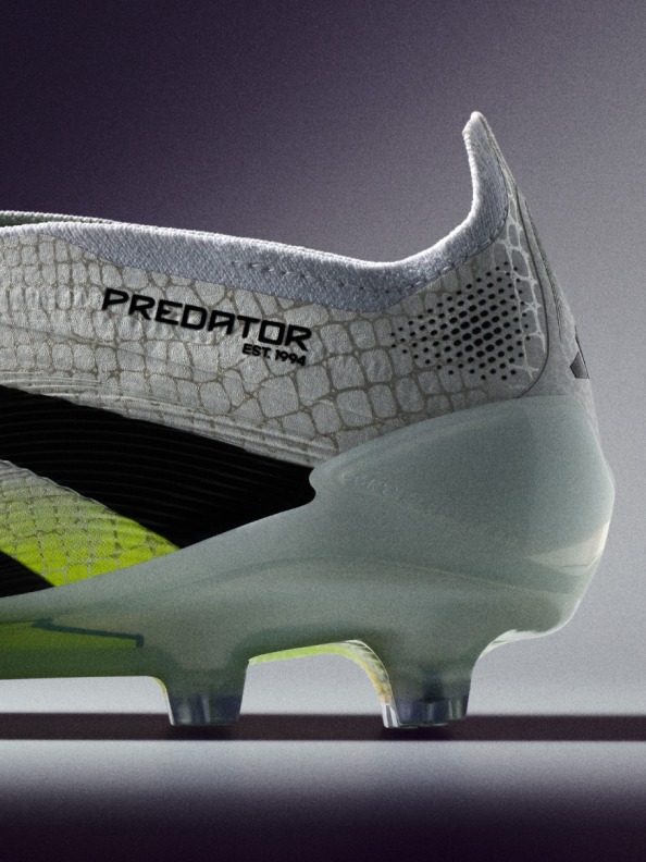 A close-up view of a white and green soccer cleat with the "Predator" logo prominently displayed, set against a dark background.
