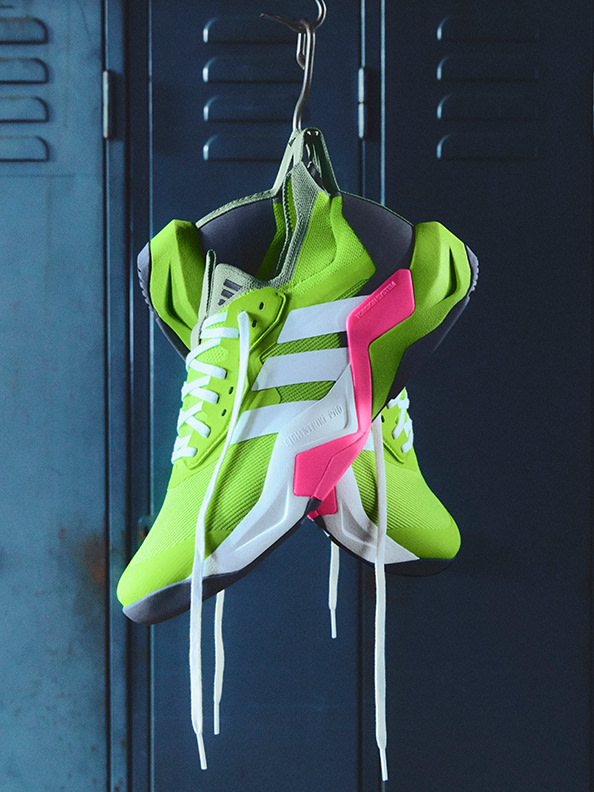 A pair of bright neon green and white athletic shoes with pink accents are hanging on a metal rack against a dark blue background.