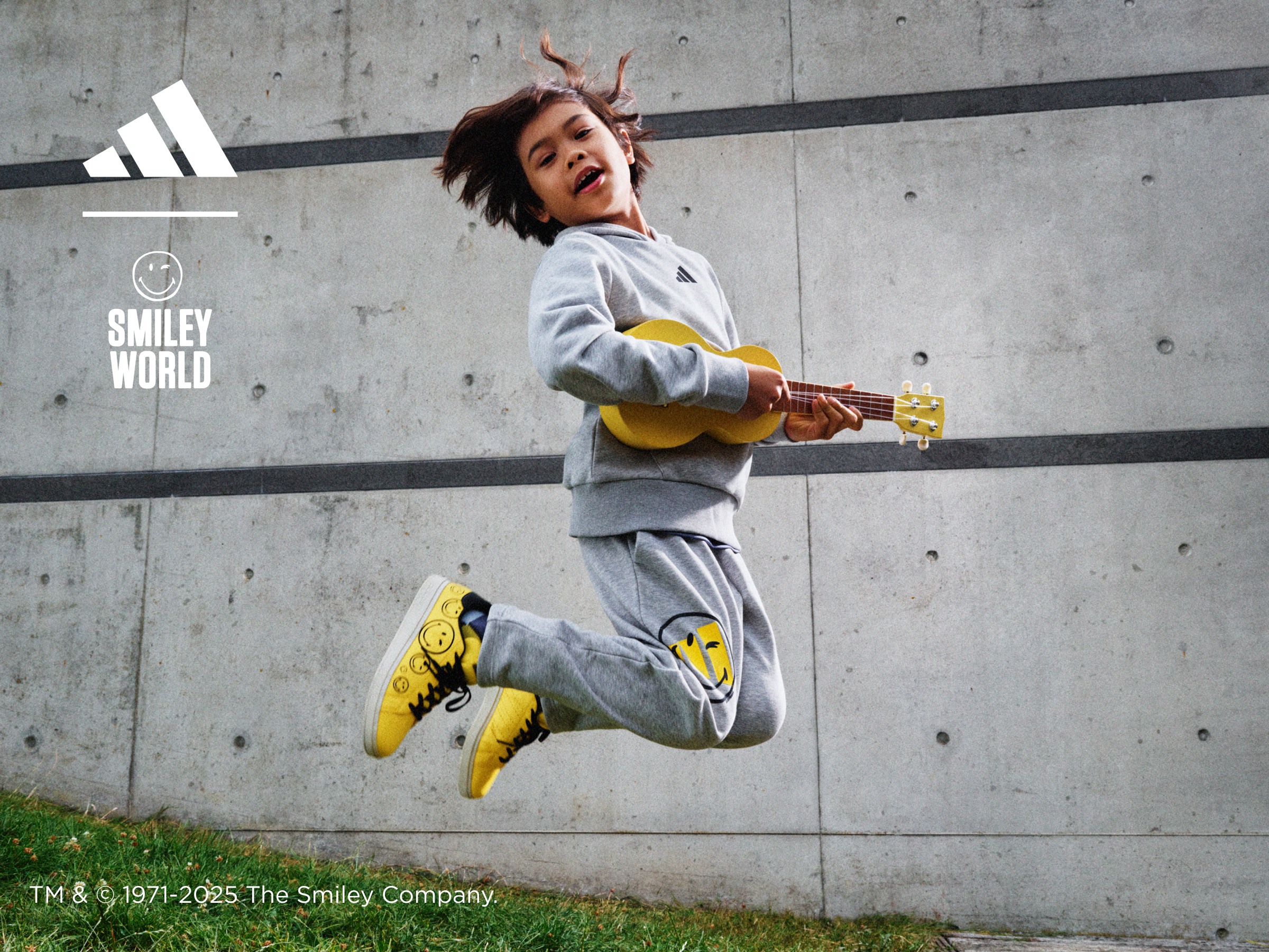 A kid wearing adidas | sportswear jumps in the air playing a ukulele.