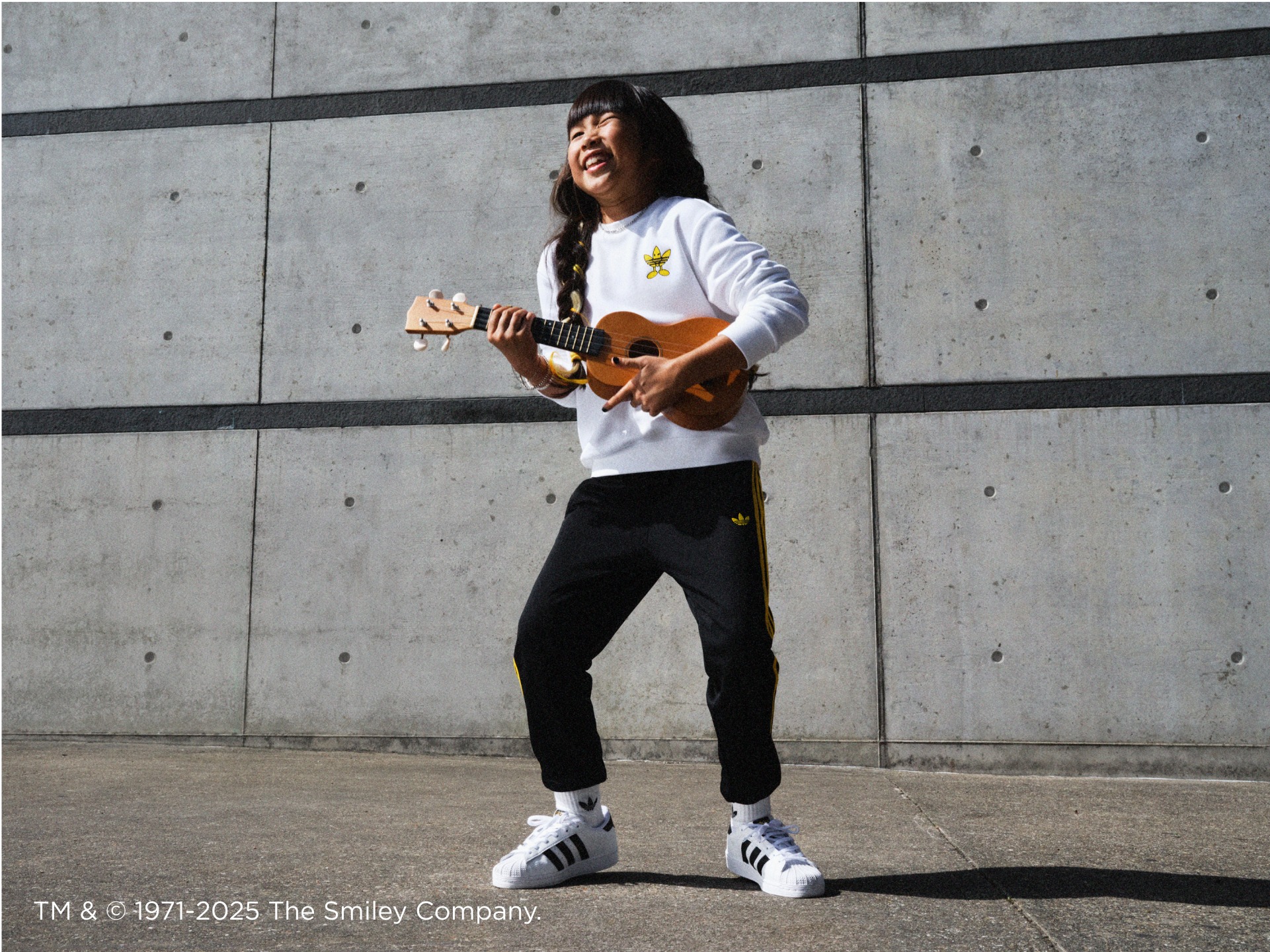 A kid wearing adidas Originals | Smiley gear plays a ukulele.