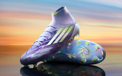 A pair of vibrant purple and green soccer cleats against a colorful sunset backdrop, creating a visually striking and dynamic composition.