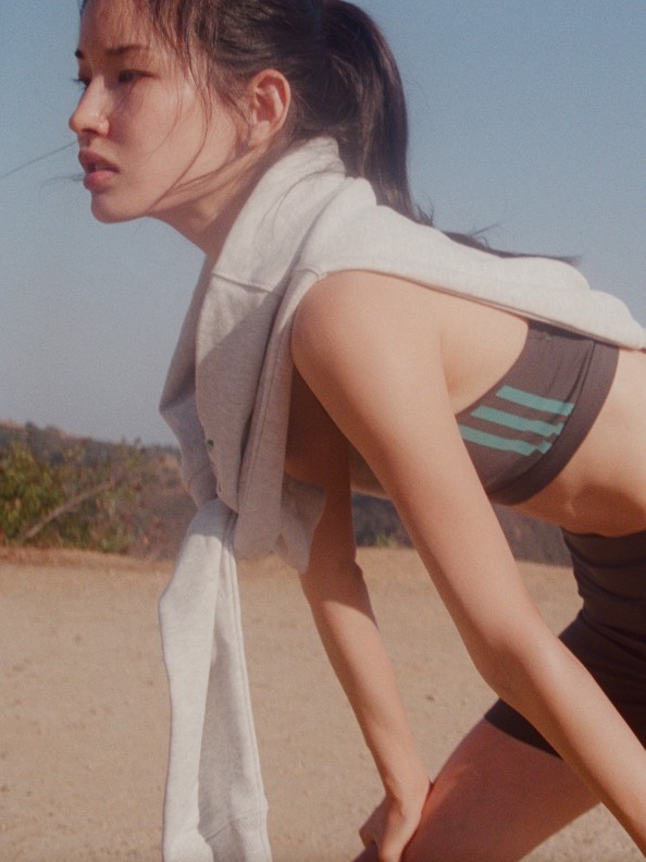 Beyaz giysili genç bir kadın, toprak bir yolda duruyor ve arka planda görünen dağlık bir manzaraya sahip.