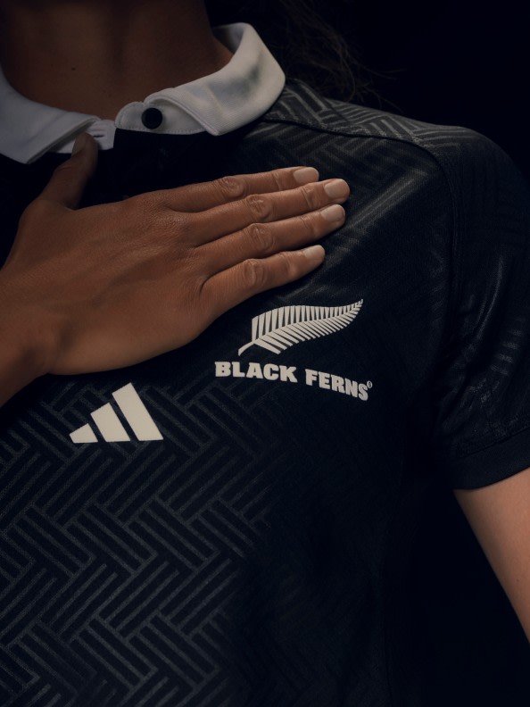 The image shows a black and white jersey with the text "BLACK FERNS" printed on it, and a hand resting on the jersey.