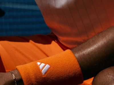 L'image montre en gros plan le bras d'une personne portant un serre-poignet de sport orange et blanc sur un fond flou de teintes bleues et orange.