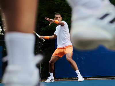 Image de Félix Auger-Aliassime portant la nouvelle chaussure adidas Barricade en blanc, sur un court de tennis, prêt à frapper un ballon.