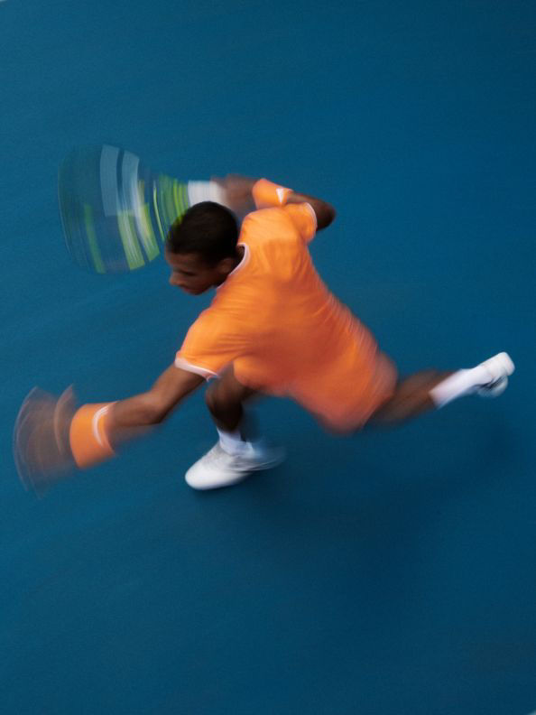 A person in an orange shirt is captured in motion against a vibrant blue background, creating a dynamic and visually striking composition.