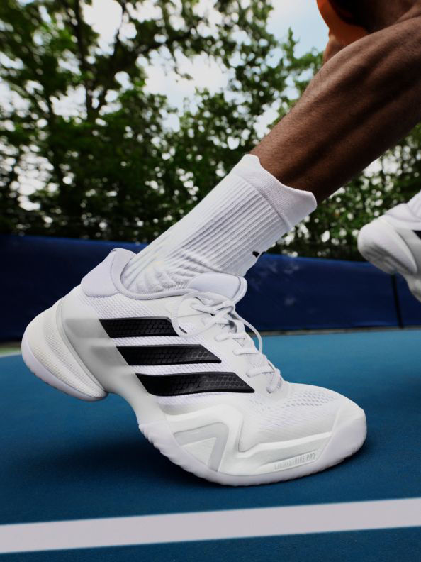 A pair of white and black athletic shoes rests on a blue surface, with a blurred green foliage background.