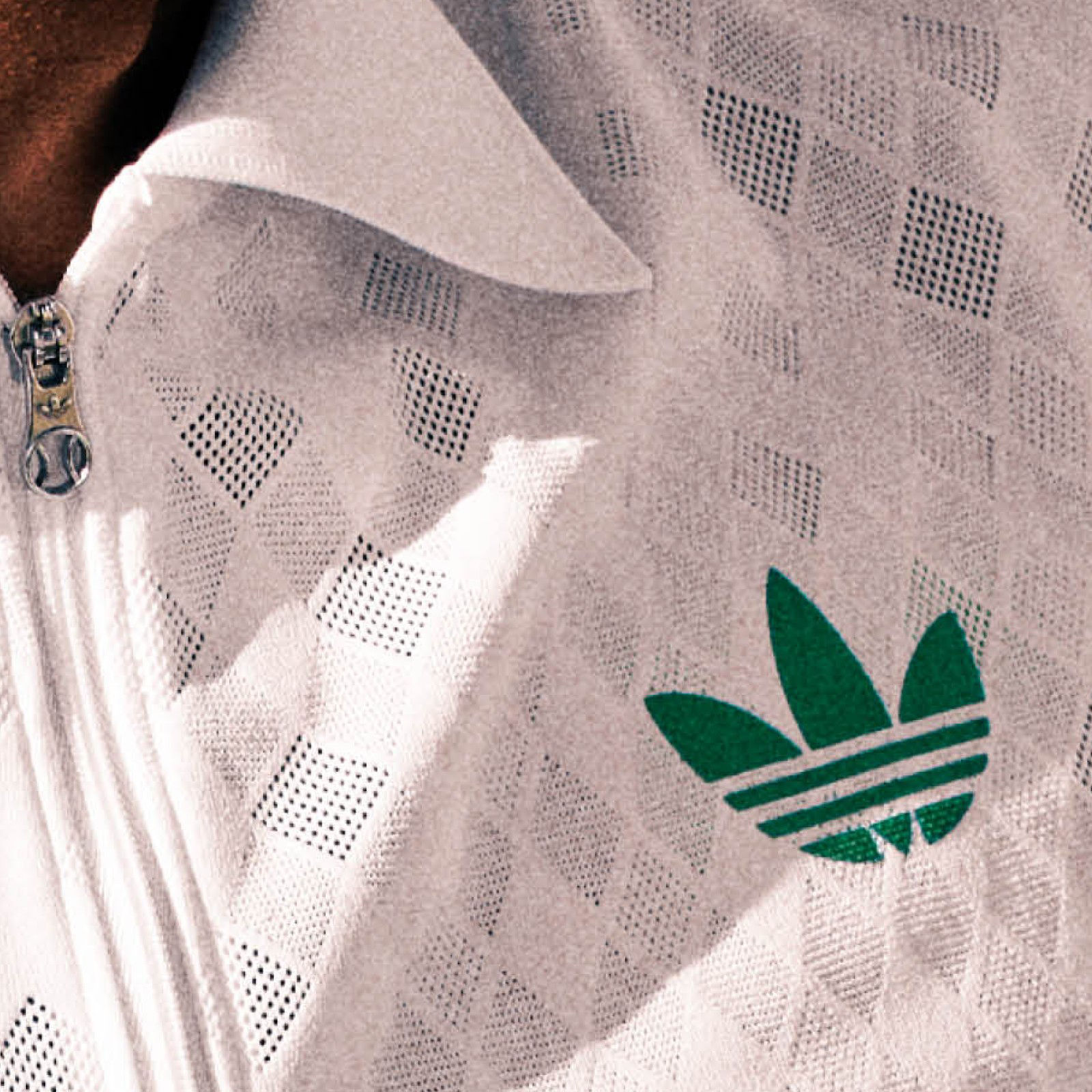 Un logo adidas blanc et vert est mis en valeur sur un tissu à motif blanc au premier plan.