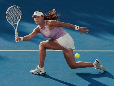 A female tennis player in a pink top and white skirt is running on a blue tennis court, with her hair flowing behind her as she prepares to hit the ball.