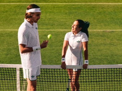 Tennis players Stefanos Tsitsipas and Camila Osorio chatting on a tennis court. They're both wearing the London Originals Collection.