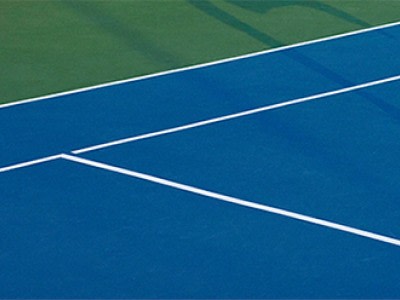 De afbeelding verbeeldt een tennisbaan met een helderblauw speeloppervlak en witte grenslijnen, tegen een achtergrond van een groen grasgebied.