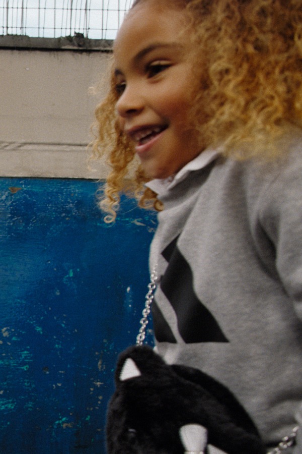 A young person with curly blonde hair smiling in front of a blue background.
