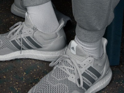 Das Bild zeigt weiße und graue adidas Sneaker mit sichtbaren Schnürsenkeln und dem adidas Logo vor einem dunklen Hintergrund.