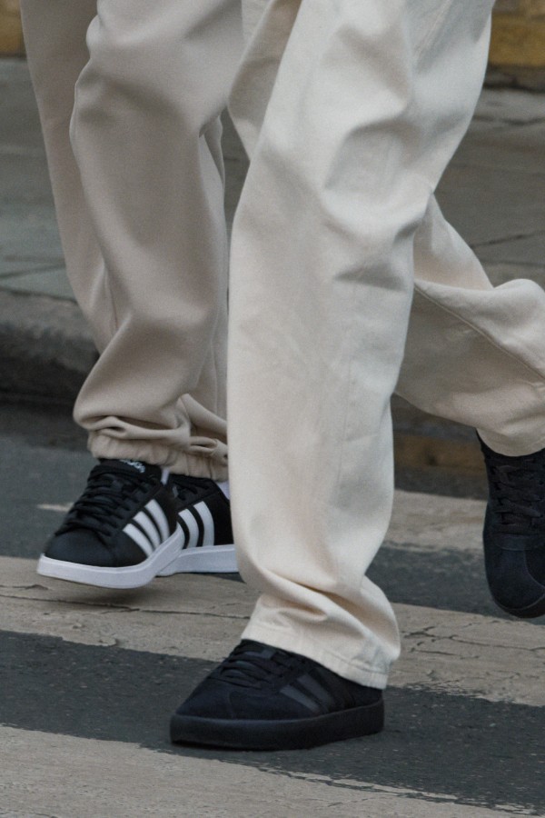 The image shows a person's lower body wearing white pants and black and white sneakers, standing on a wooden platform against a blurred background.
