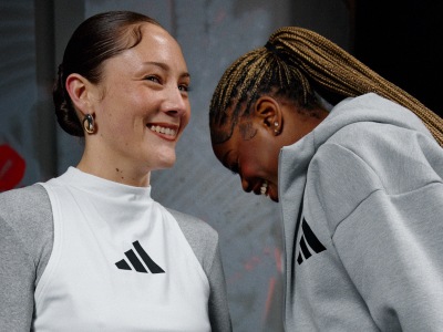 The image shows two people, a woman with a warm smile and a man with braided hair, standing close together and appearing to have a friendly conversation.