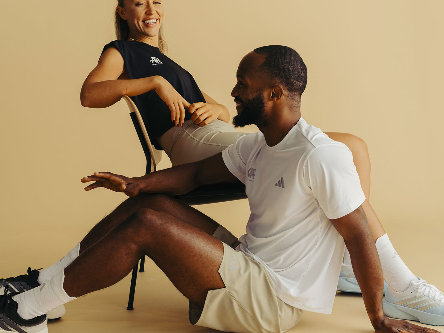 A woman in a black athletic top and a man in a white shirt are sitting together, with the woman appearing to be assisting or interacting with the man.