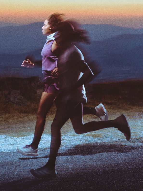 Two people are running together on a road at sunset, with mountains visible in the background.