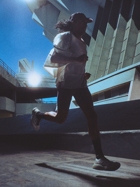 A person in athletic clothing is running on a concrete surface, with a modern building and bright sky visible in the background.