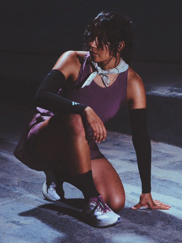 A person in athletic clothing is crouched on a dark stage, appearing pensive or contemplative.