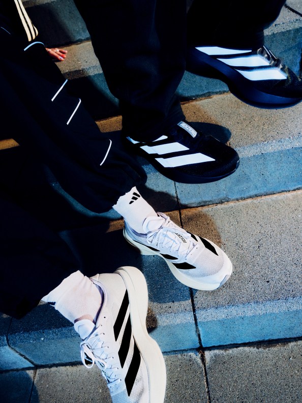 The image shows a close-up view of a person's feet wearing black and white athletic shoes, standing on a concrete surface with painted lines.