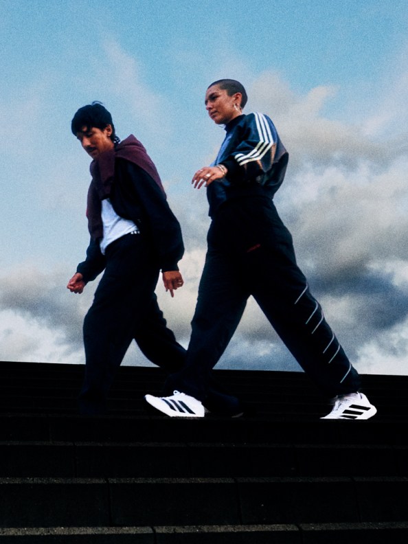 Two individuals wearing athletic clothing are running on a raised platform against a cloudy sky backdrop.