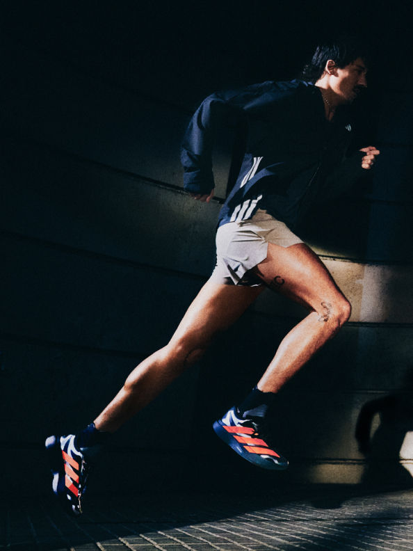 A person in athletic clothing is crouched down on a dark surface, with their legs and feet visible in the foreground.