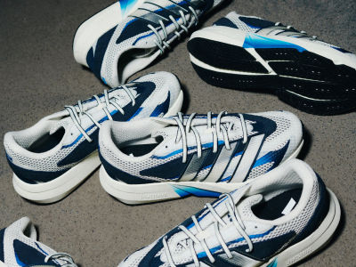 A pair of white, blue, and black athletic shoes with laces and treads visible, resting on a dark surface.