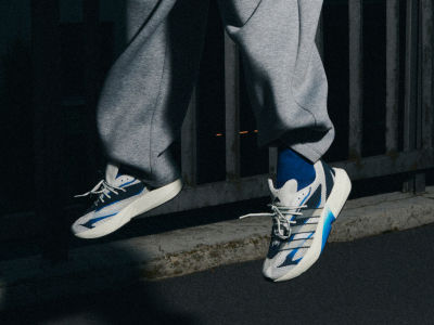 The image shows a person's legs and feet wearing a pair of white and blue sneakers, standing on a dark surface in a dimly lit environment.